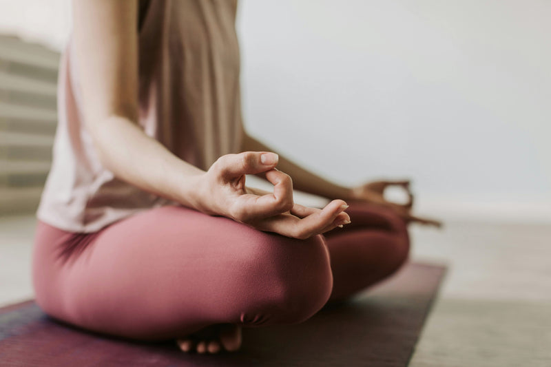 Person sitting in a yoga pose on a mat with a blurred background